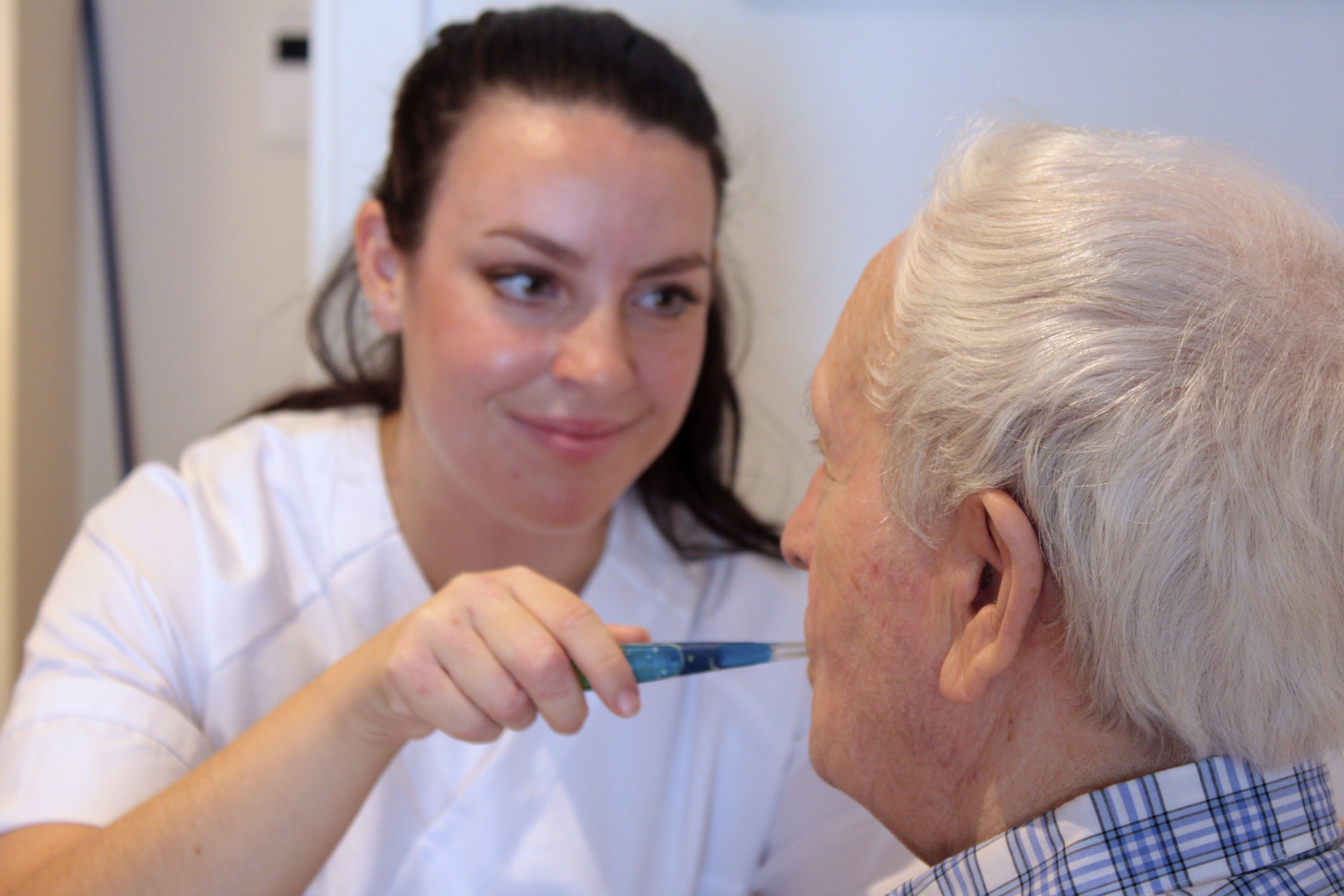 Sykepleier utfører munnstell på en eldre mann Bildet viser en sykepleier som pusser tennene til en eldre mann