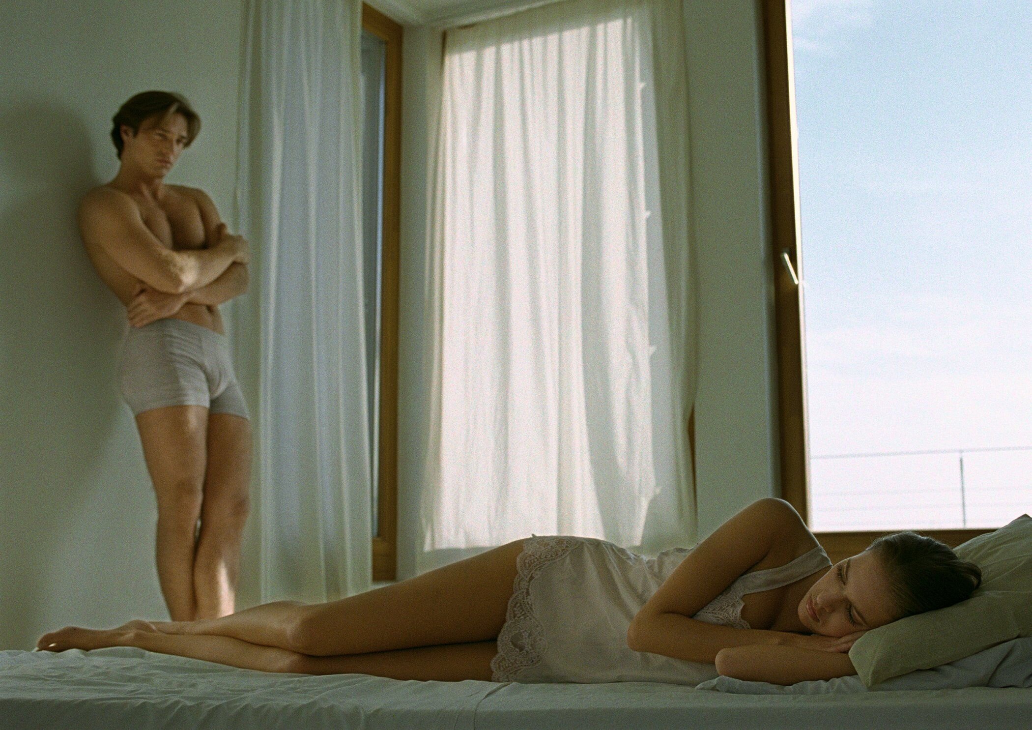 Kjærester En mann og en kvinne på soverommet. Mannen står inntil en vegg og ser misfornøyd ut.