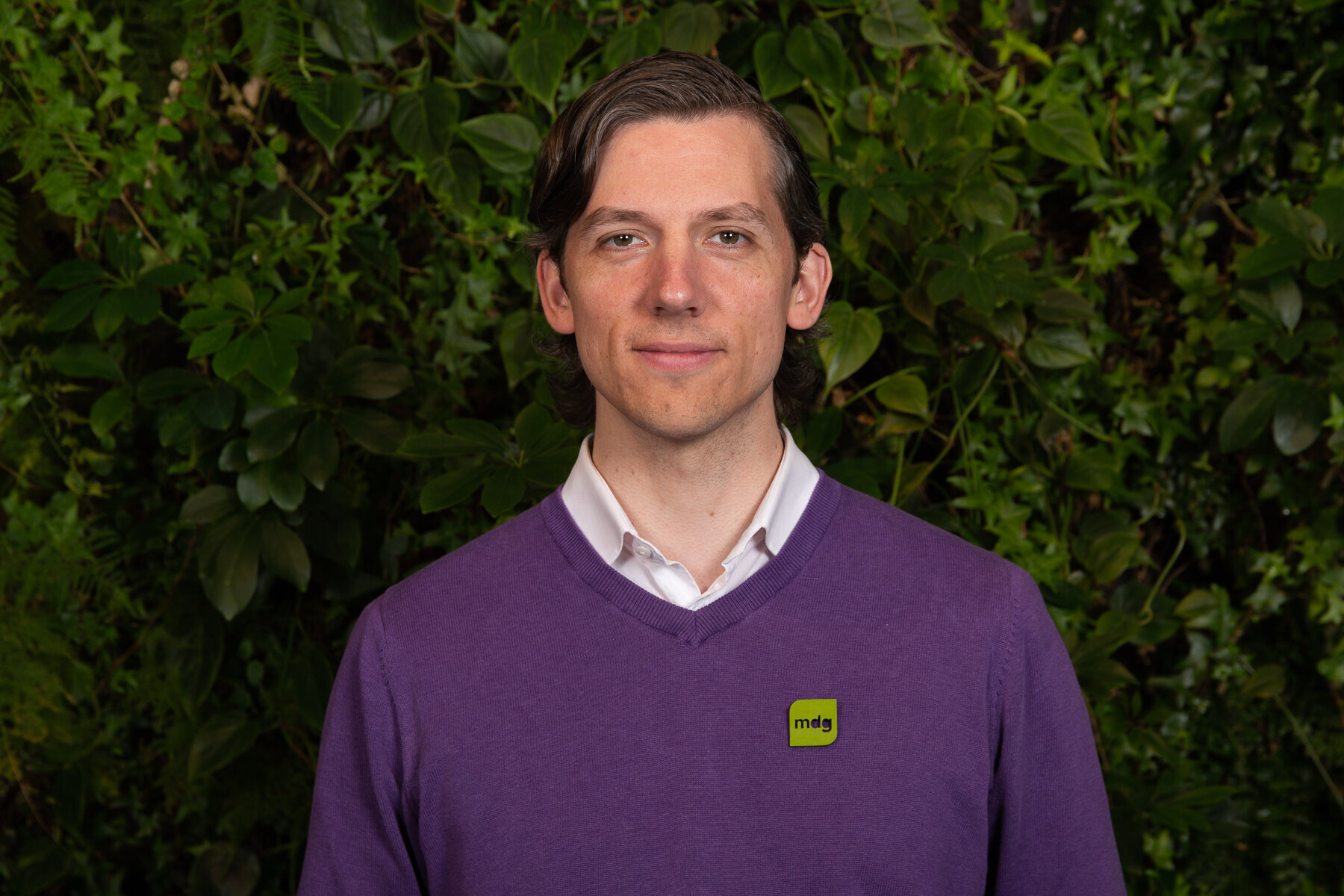 Ung mannlig politiker i hvit skjorte og lilla genser foran grønn busk