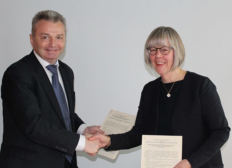 Anne Grethe Erlandsen og Igor Kagramanyan gir hverandre et håndtrykk mens de holder programmet de har signert