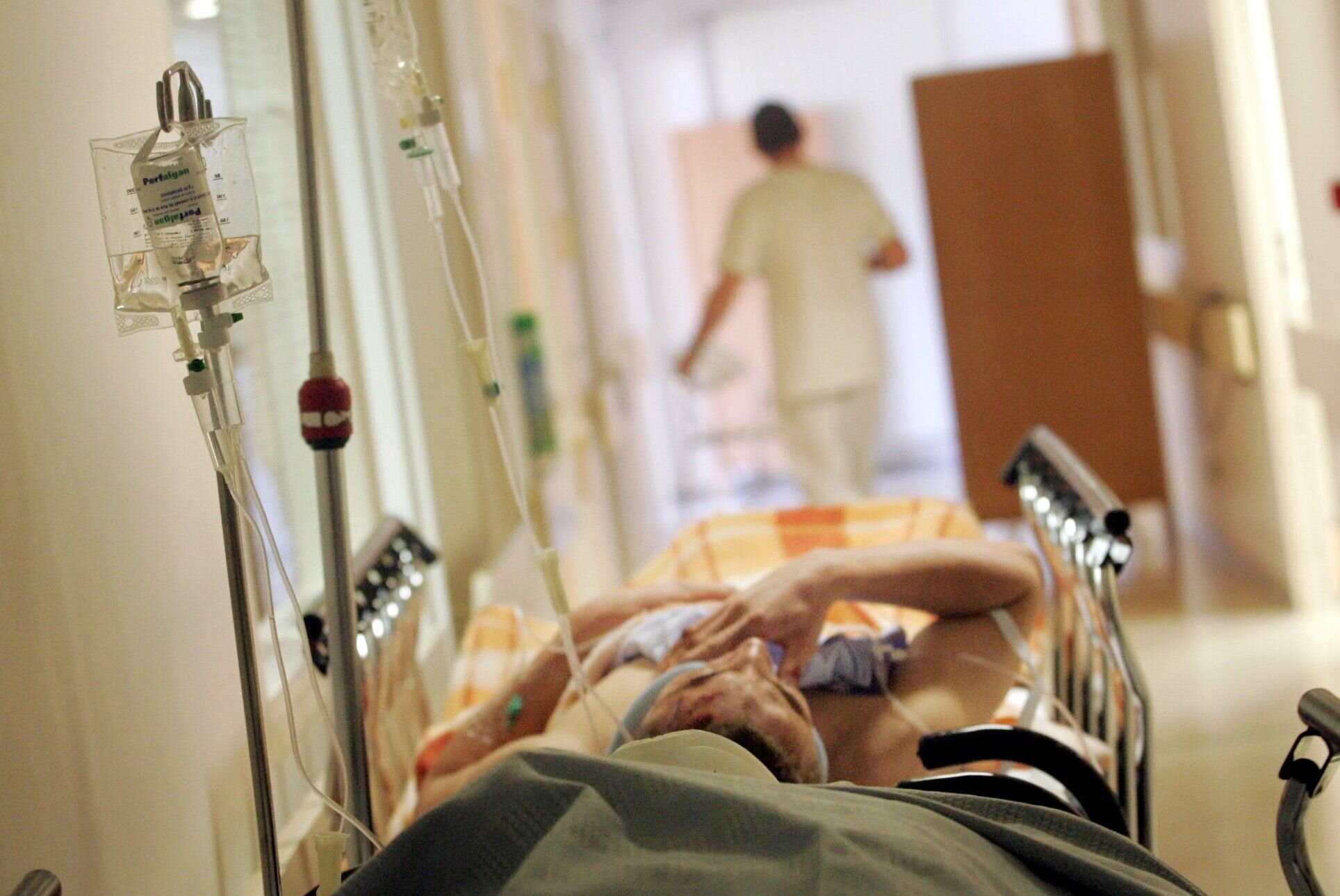 Korridorbilde fra sykehus hvor det ligger en pasient. Helsepersonell går bortover