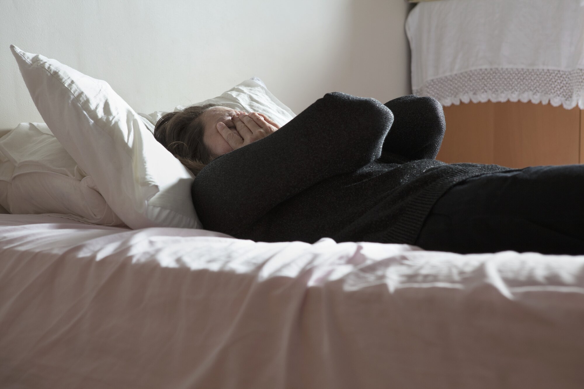 Deprimert kvinne på seng Bildet viser en deprimert kvinne som ligger på en seng og holder hendene foran ansiktet