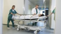 Bildet viser en pasient i en sykehusseng som blir trillet av helsepersonell