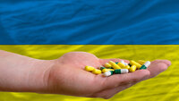 Bildet viser en hånd som holder piller, i bakgrunnen ses litt av det ukrainske flagget.