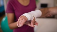 Dette er et nærbilde av en bandasjert hånd med en pleier i bakgrunnen.
