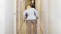 Bildet viser en eldre dame som går bortover en sykehjemskorridor
