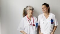 Bildet viser en ung og en eldre sykepleier som smiler til hverandre.