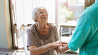 Bildet viser en hjemmeboende eldre kvinne som smiler til en sykepleier.