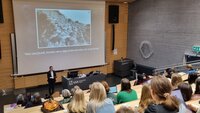 Bildet viser en foreleser som står foran mange studenter Bildet viser en foreleser som står foran mange studenter