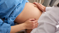 Bildet viser en gravid dames mage. Hendene til en lege eller sykepleier undersøker magen