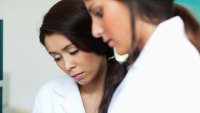 Sykepleierstudenter Bildet viser to kvinnelige sykepleiere som har ikke-etnisk norsk opprinnelse, som står og ser på noe sammen.