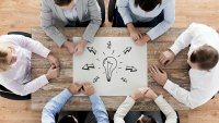 Samarbeid Bildet viser seks personer som sitter rundt et bord, på bordet ligger det en tegning av en lyspære med piler rundt til alle kanter.