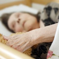 Gammel dame ligger i en seng.