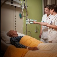 Bildet viser en veileder og sykepleierstudent ved en pasient i senga