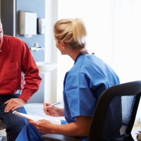 Bildet viser en mannlig pasient som er i konsultasjon med en kvinnelig sykepleier. Han sitter på en sykehusseng, og hun har et skjema i hånda.