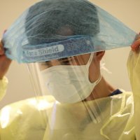 Bildet viser en mann som tar på seg beskyttelsesutstyr, som maske, visir, smittefrakk osv.