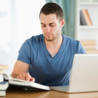 Bildet viser en mannlig student som leser i bøker og skriver på en laptop