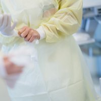 Bildet viser helsearbeidere i gule frakker som tar på hansker.