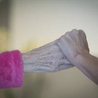 Bildet viser en sykepleier som holder et eldre menneske i hånden