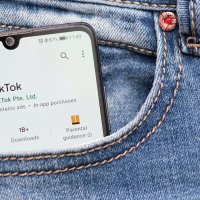 Bildet viser en mobil med TikTok som stikker opp av en bukselomme.
