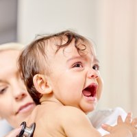 Bildet viser et lite barn som gråter mens en sykepleier lytter på ryggen til barnet