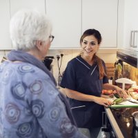 Bildet viser en kvinnelig sykepleier som smiler og snakker med en eldre kvinne