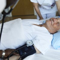 Bildet viser en sengeliggende mannlig pasient som får pleie av to sykepleiere