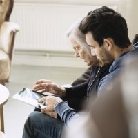 Bildet viser en eldre dame på sykehjem som ser på et nettbrett sammen med en pleier