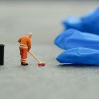 Bildet viser en miniatyrmann som koster opp rundt en engangshanske av plast