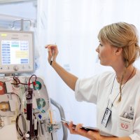 Bildet viser en intensivsykepleier som trykker på en skjerm på en maskin med masse slanger og annet utstyr