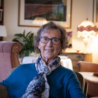 Signy Romslo sitter hjemme i soffa og siler til kamera