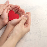 Bildet viser et par damehender som holdt rundt et par barnehender. Barnet holder et hjerte i sine hender.