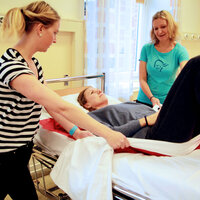 Bildet viser bedriftsfysioterapeutene Anne Aschehoug Loftu og Sigrunn Haug Simensen viser hvordan man ved hjelp av forflytningsteknikk kan flytte «pasient» Gina Grøtting Sjöström oppover i sykesengen på en mindre belastende måte.