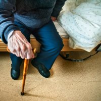 Bildet viser hånden til en gammel mann som støtter seg til en stokk.